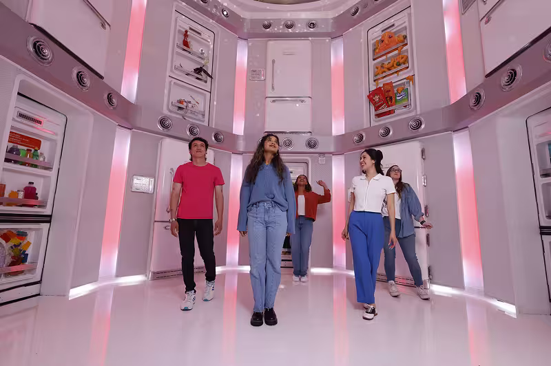 Five people standing inside a room with white walls and red lights, featuring shelves with colorful items.