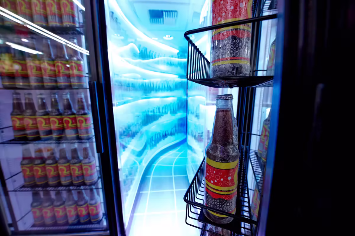 Frozen bottles with red and yellow labels inside a lit glass-door cooler with icy walls and floor.